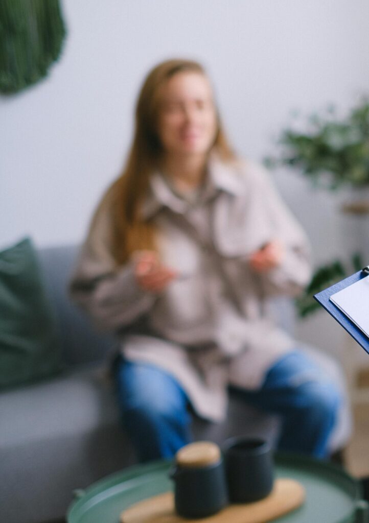 Unrecognizable professional female psychologist writing on clipboard while sitting against client on blurred background during psychotherapy session in light office