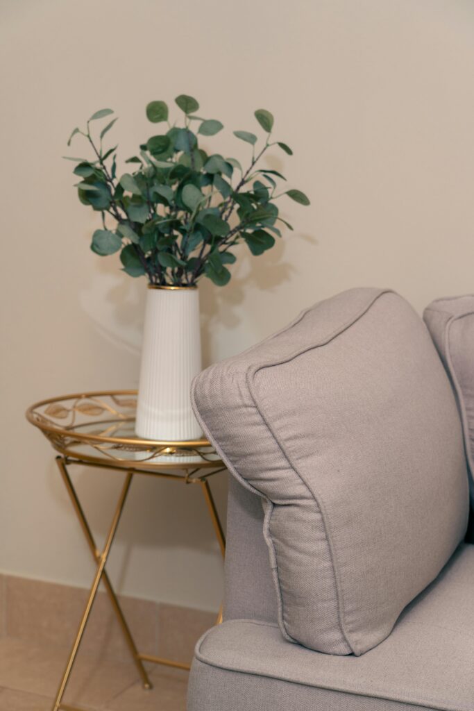 A stylish grey couch paired with a decorative vase of foliage on a modern gold side table.